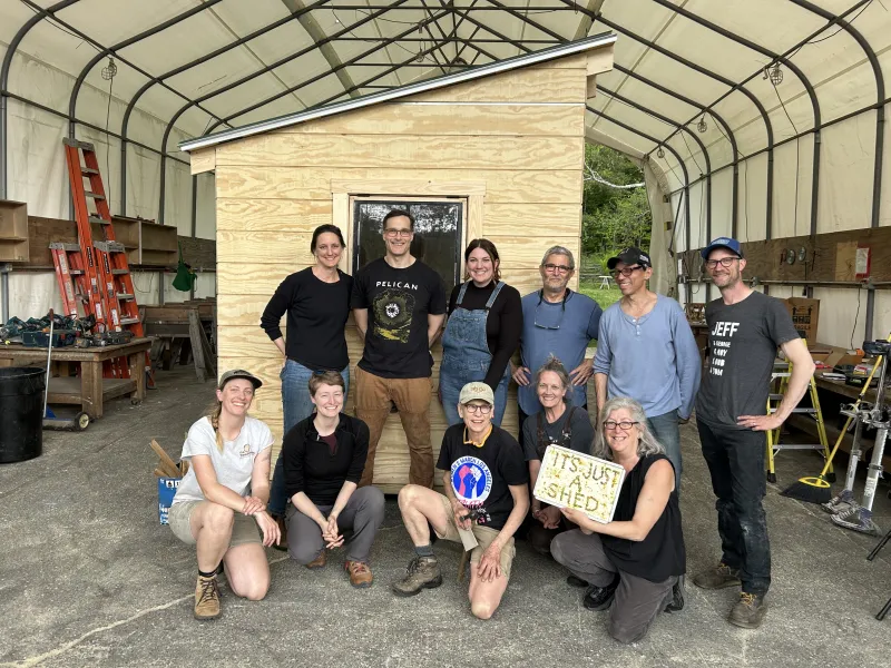 A group of twelve people poses for a photo in front of their garden shed.