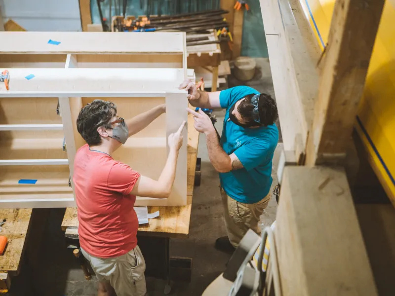Two people working on a set of kitchen cabinets.
