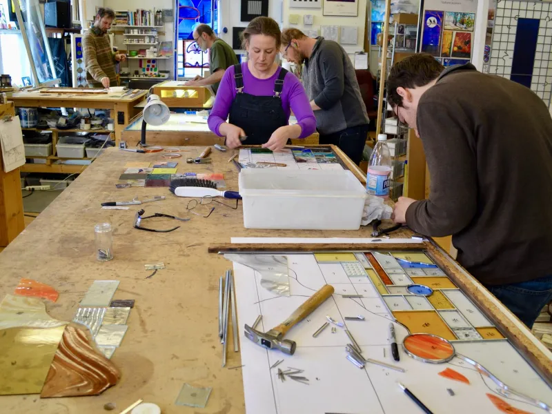 Students at a workbench assemble stained glass pieces.