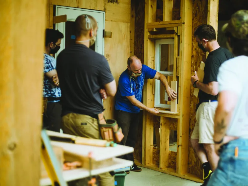 A person demonstrates on a trimmed window opening inside a framed structure.
