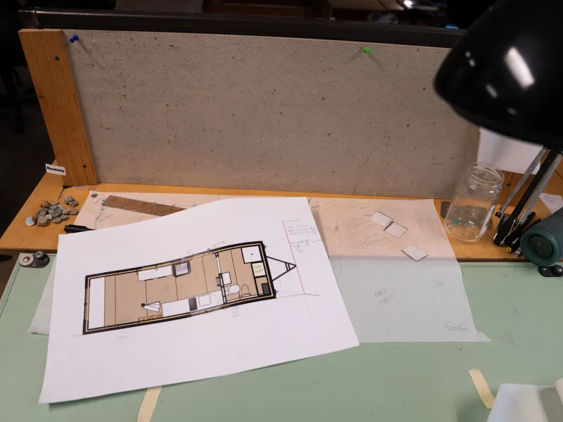A sketchup model of a tiny house lies on a drafting table