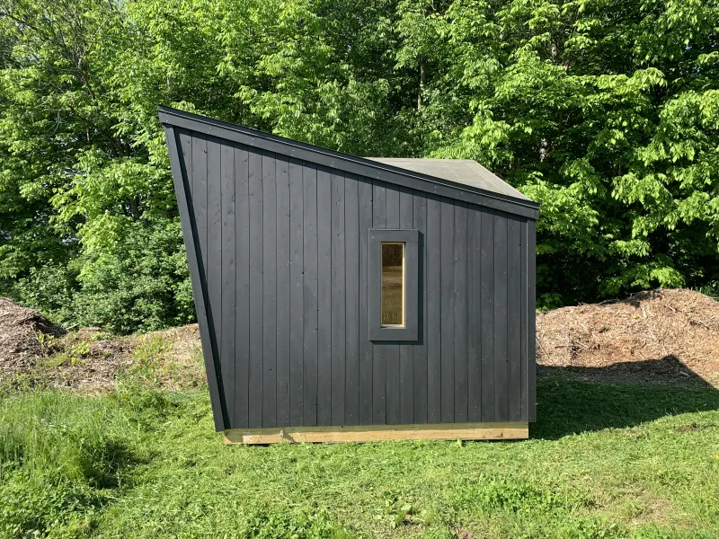 The exterior of a sauna with black siding and a steep angle roof. 