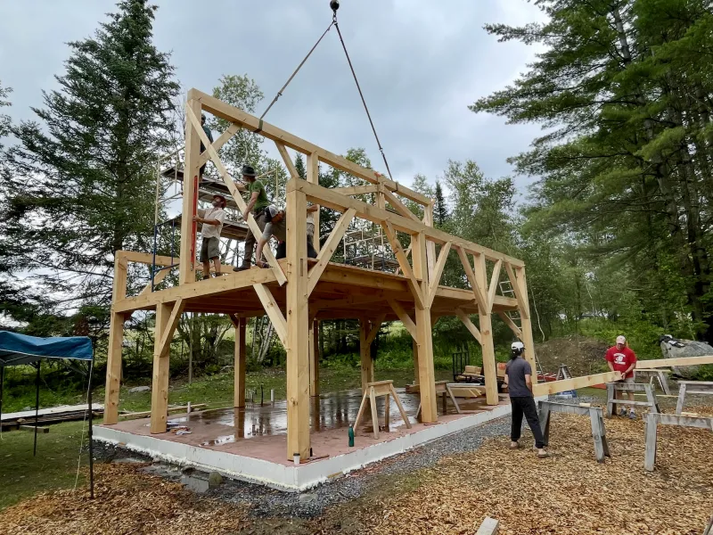 A timber frame ridge beam is raised by a crane