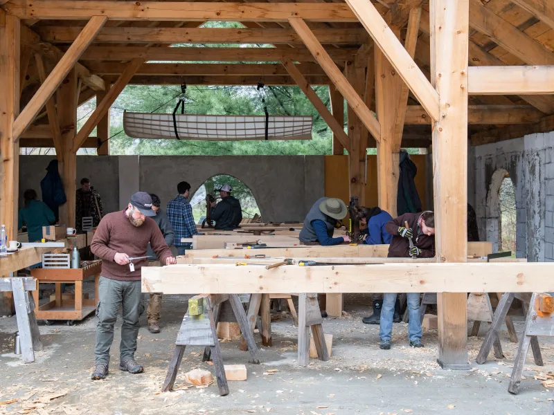 Students work on cutting joinery on timbers in an outdoor classroom