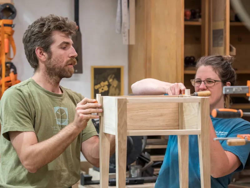 Two people work on a side table in the woodshop.