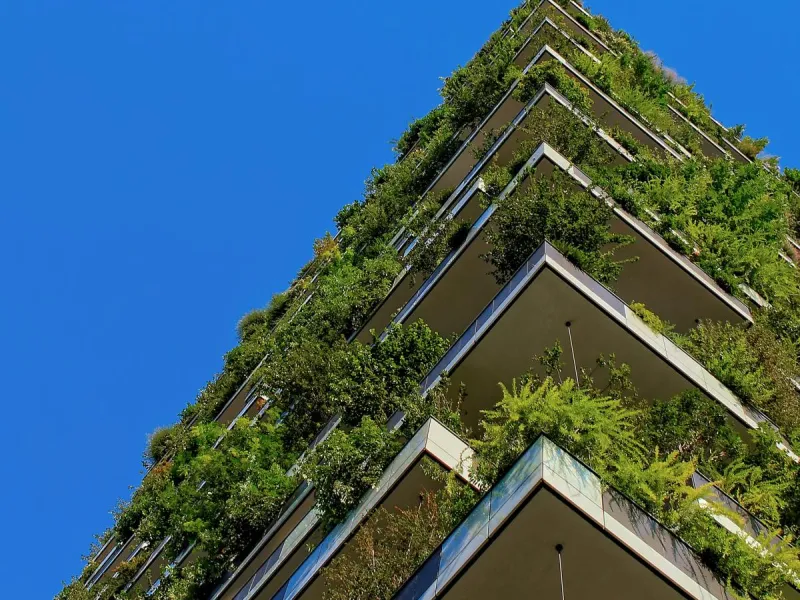Photo looking upwards at the corner of a building with several balconies abundant with plants. 