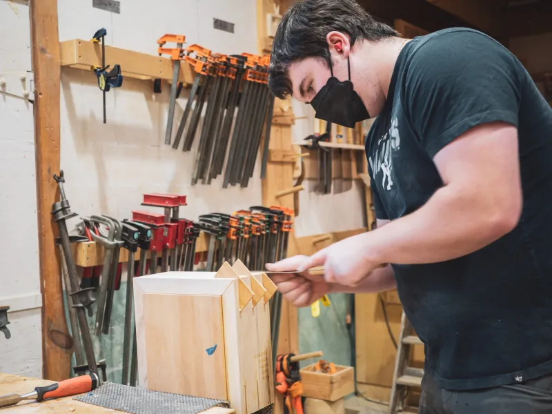 A student uses a pull saw to cut splines on a box. 