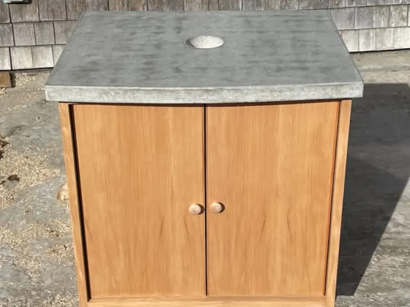 A douglas fir wood bathroom vanity cabinet with a gray concrete countertop with a drain opening to accomadate a vessel sink. 