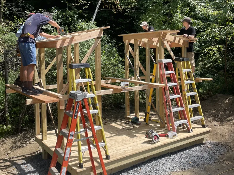 Students standing on a wooden platform adding the roof structure to a carpentry project.