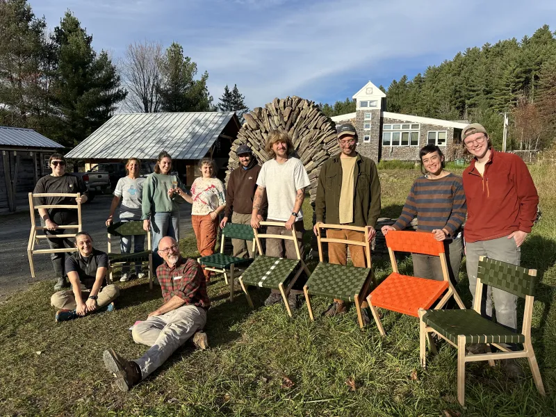 A group of students poses outside with the chairs they made.