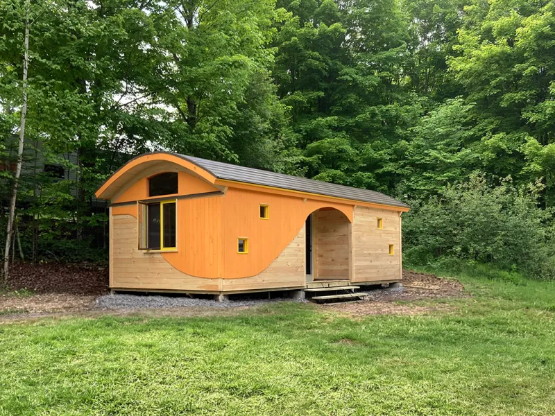 A cabin with a curved roof, pine shiplap siding and orange accents.