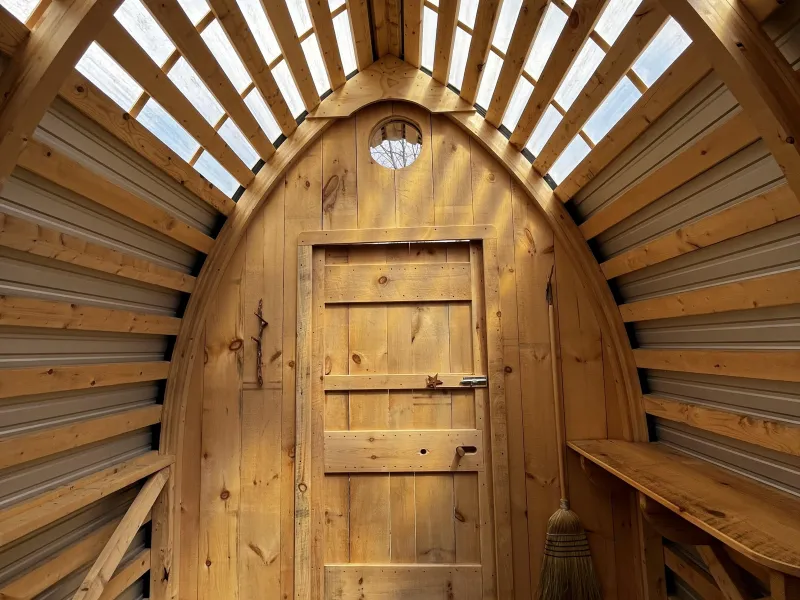 The interior of a project completed by the 2024 Collaborative Design/Build Intensive featuring wood siding, a curved roof and clear roof panels.
