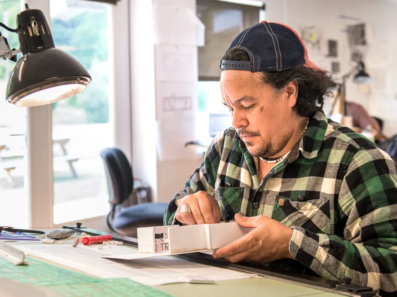 A student sitting at a drafting table and building an architectural model. 