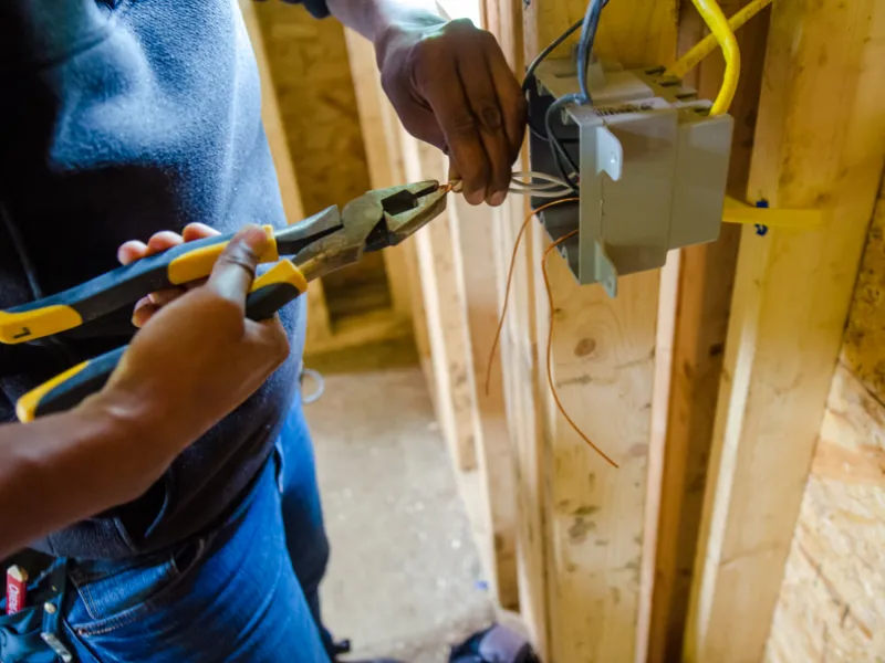 A close up of hands holding needle nose pliers and wiring an outlet box.