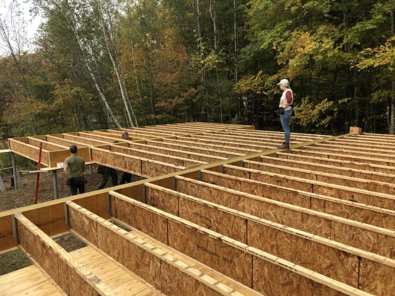 A floor deck is being framed with joists exposed and trees in the background.