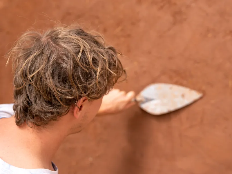 A student is photographed from behind plastering a wall with a trowel.