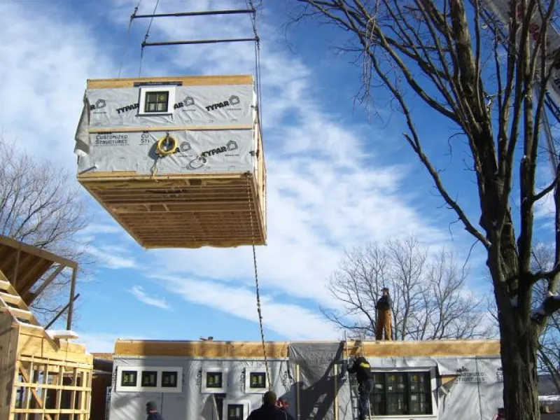 A module of a pre fabricated home wrapped in house wrap and suspended from a crane.