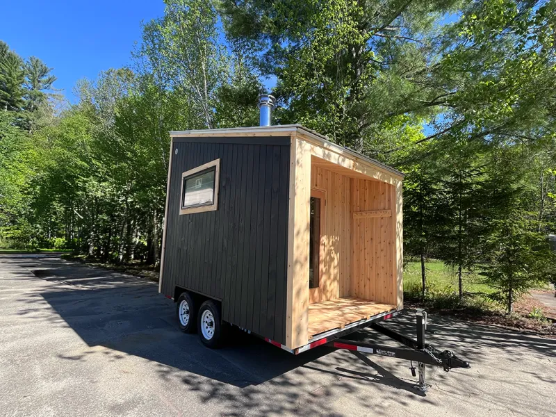 Exterior of a mobile sauna with dark siding and cedar trim. 