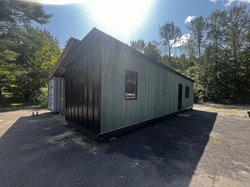 The exterior of a shipping container home clad in teal shiplap siding and black metal.