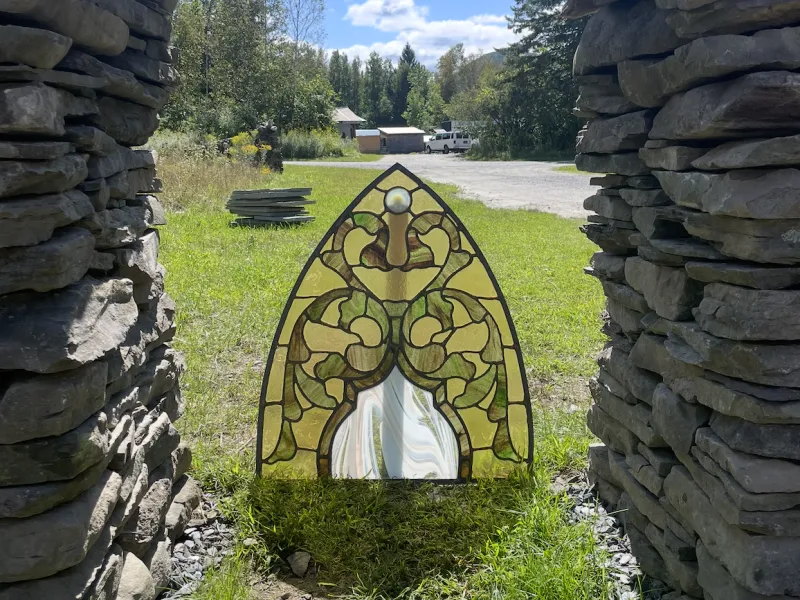 A stained glass panel in an arch shape is pictured outside.