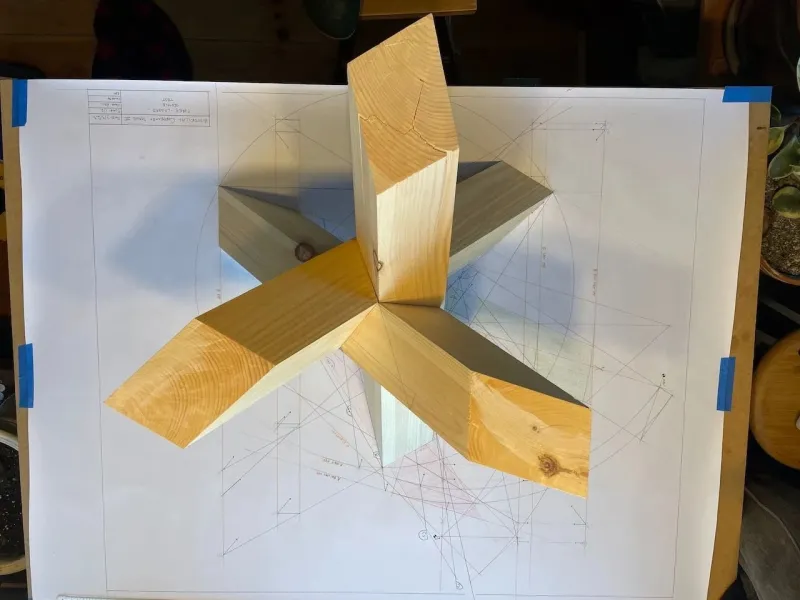A wooden model of a three legged trestle set on top of hand drawn plans. 