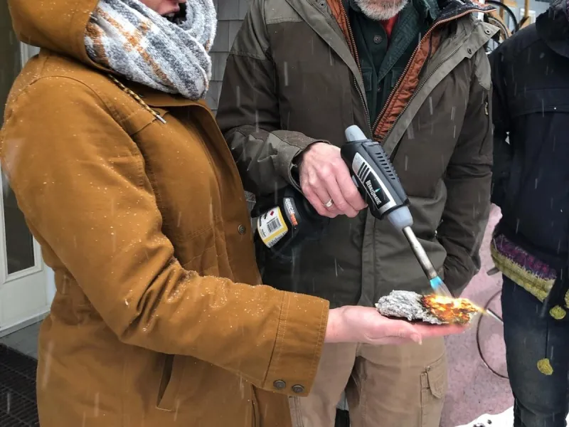 A student holds a piece of insulation while an instructor torches it, without hurting the student's hand (the student looks surprised and delighted)