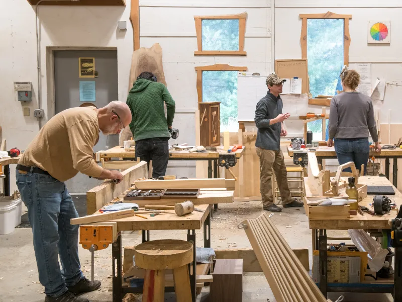 Several people are pictured in a wide shot of the woodshop. 