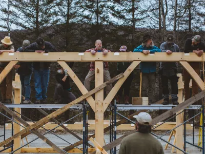 A timber framing class raises the ridge beam of the structure, while the instructor looks on.
