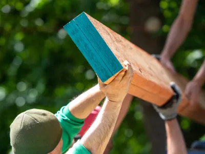 Several people work together to lift a beam into place on a jobsite.