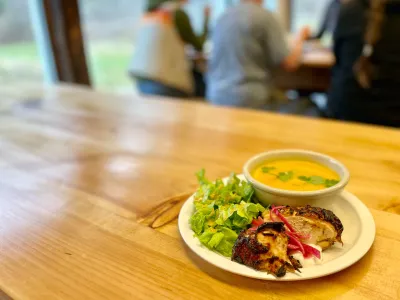 plate of food on wood table in the foreground, students eating at a table in the background