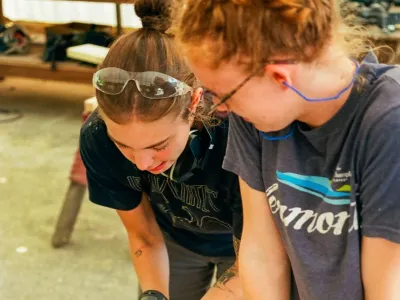 Two students work together on cutting a board, one is holding and the other is preparing to cut with a circular saw.