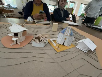 Several paper models are photographed in the studio on a topographic cardboard site model.