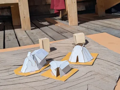 Several paper models are photographed outside on a wooden deck.