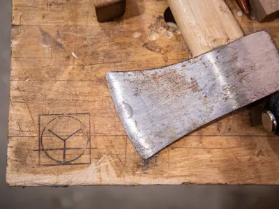 close up shot of an axe head lying on a wooden benchtop with yestermorrow logo burned into it.