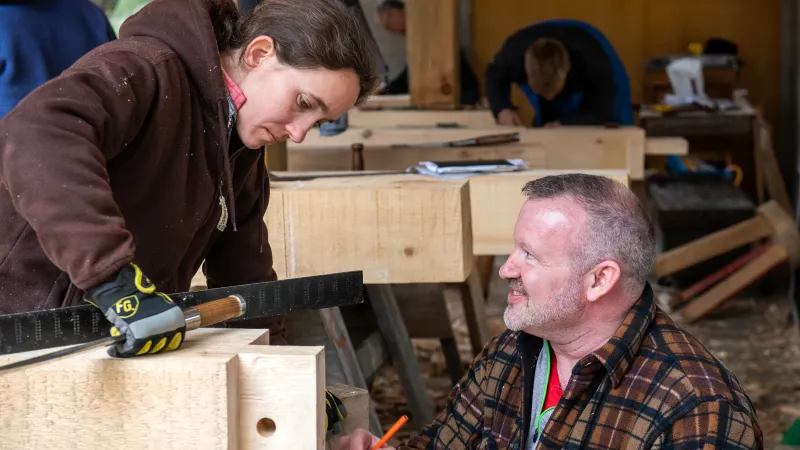 Two people work on a timber frame tenon.