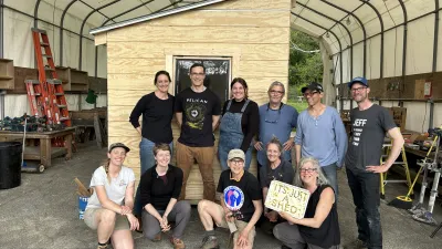 A group of twelve people poses for a photo in front of their garden shed.