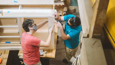 Two people working on a set of kitchen cabinets.