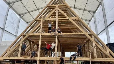 A group of carpenters poses in front of several-story-high trusses assembled in an indoor building space.