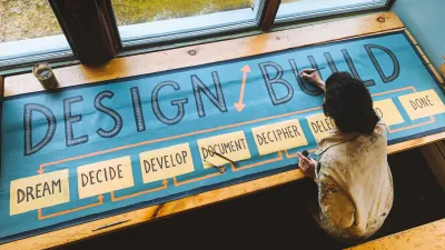 A photo from above of a dark haired woman painting a banner that says "Design/Build" with the steps of the design/build process below