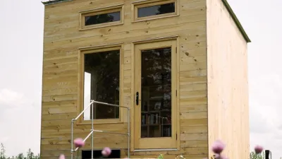 A finished tiny library stands in a field with sky in the background and red clover in the foreground.
