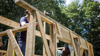 Two people work on framing a building with trees and sky in the background