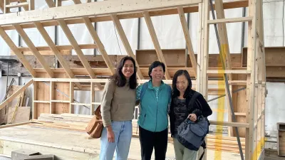 Three women of varying ages stand in front of a framed structure in an outdoor tent