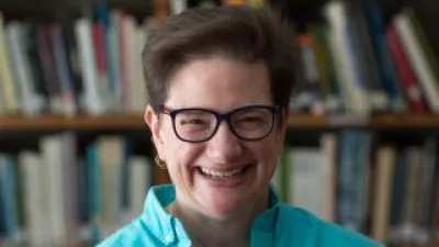 Michelle Lee smiles in front of bookshelves. She has short brown hair, glasses, and a turquoise collared shirt.