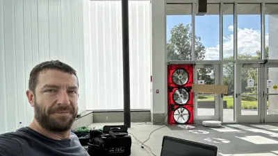 Nate is pictured looking at the camera with a blower door test being conducted in the background of a naturally lit building