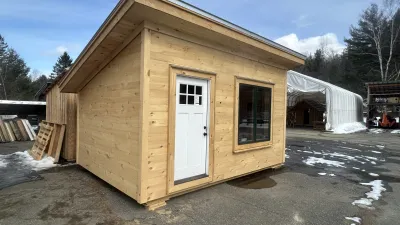 The exterior of a cabin with a large window, white door, pine shiplap siding and a shed roof.
