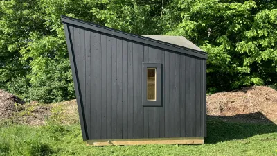 The exterior of a sauna with black siding and a steep angle roof. 