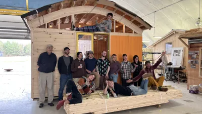 A group of students poses for a photo in front of a small cabin with curved roof and orange details.