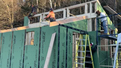 Several people working on a framed and partially zipped building