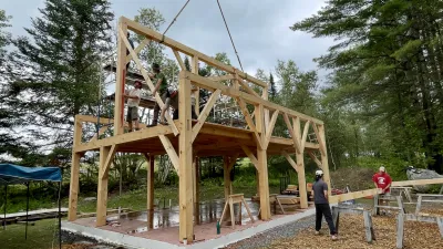 A timber frame ridge beam is raised by a crane