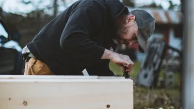A student pictured outside on the pavement uses a combo square on a timber frame tenon.